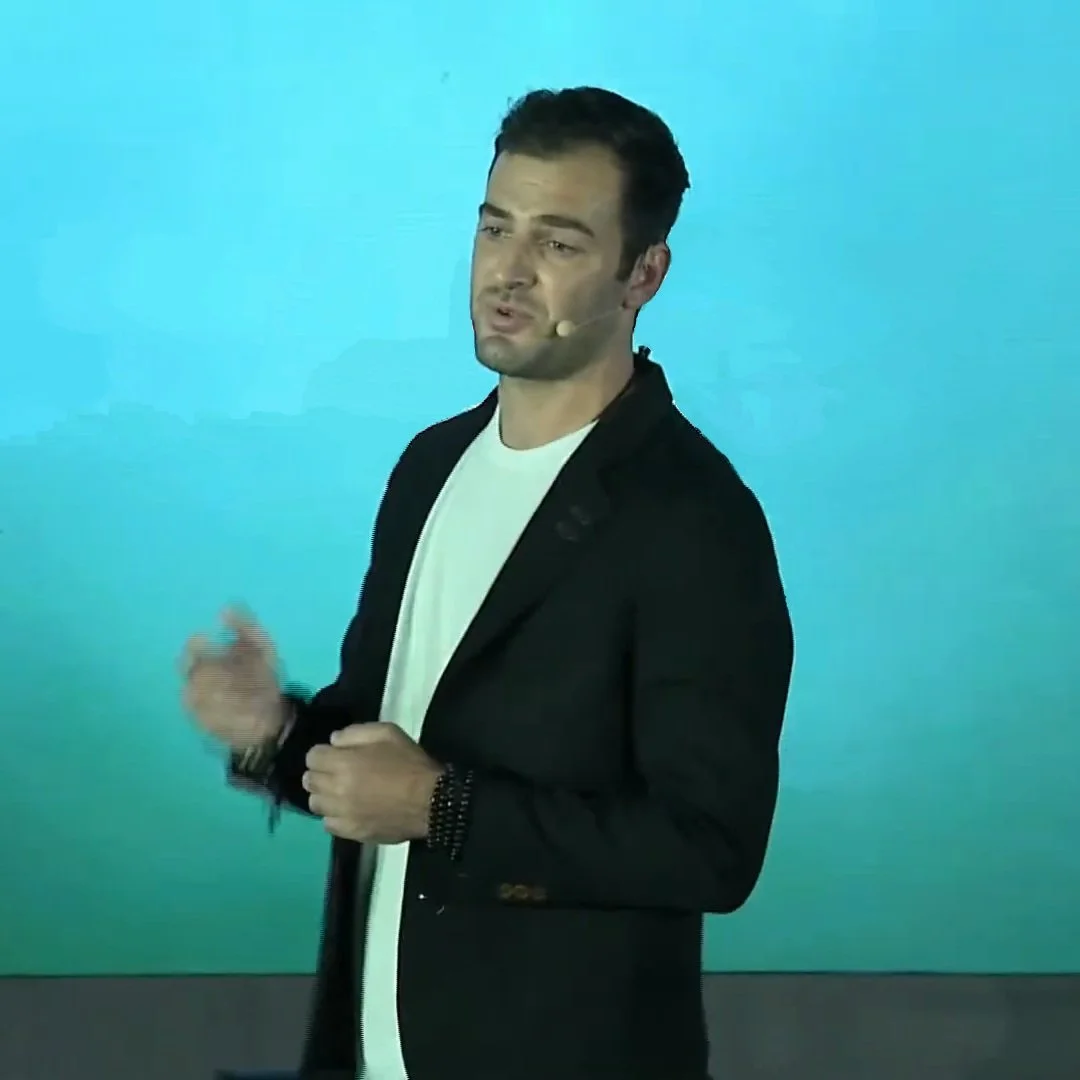 Grant Kendzior speaking on stage wearing a headset microphone